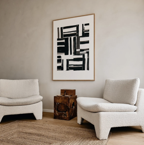 Twee lichte fauteuils met een kunstwerk aan de muur en een houten bijzettafel.